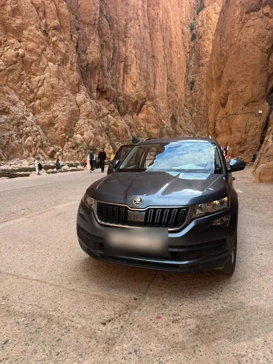 A grey SUV on the road through a narrow red rock gorge, in Morocco