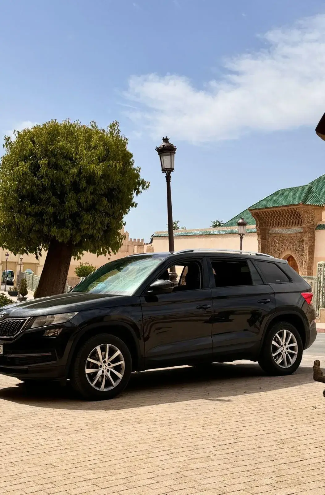A black SUV parked in front of a carved gate with a green tiled roof, in Morocco